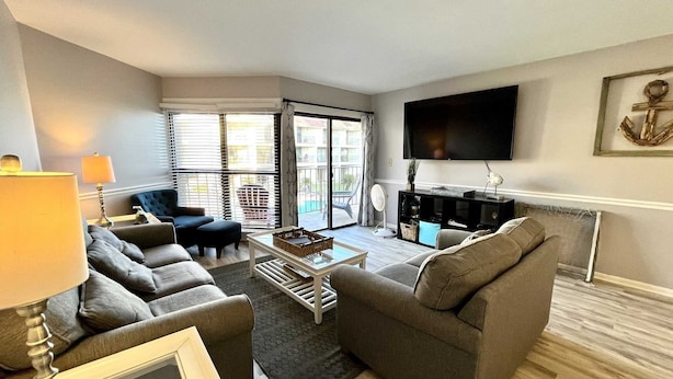A living room with a sofa set, a coffee table, and a TV mounted on the wall. - Gulfside Townhome 13 2 Bedroom Townhouse by RedAwning (Gulf Shores)