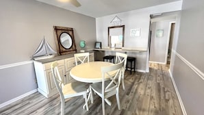 A compact kitchen with a round table and white chairs, a ceiling fan, and a small sailboat model. - Gulfside Townhome 13 2 Bedroom Townhouse by RedAwning (Gulf Shores)
