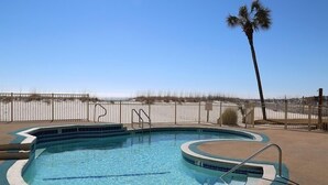 Une piscine à bord incurvé, entourée d’une zone sablonneuse et d’une clôture en bois.