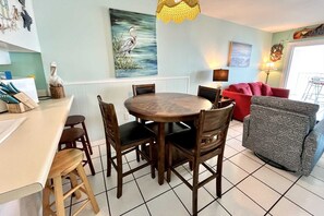 A dining area with a round wooden table and chairs, a red sofa, and a grey armchair. - Harbor House B2 2 Bedroom Condo by RedAwning (Gulf Shores)