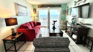 A living room with a red sofa, patterned armchair, and a small table with a lamp. A wooden cabinet and a decorative fish on the wall are also visible. - Harbor House B2 2 Bedroom Condo by RedAwning (Gulf Shores)