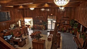 A spacious, wooden-furnished living area with a large TV, multiple seating options, and a variety of plants.