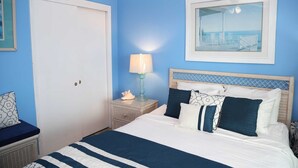 Un dormitorio con cama, mesita de noche, lámpara y un cuadro en la pared.