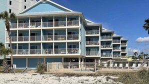 Un hotel frente al mar de varios pisos con balcones, un área de piscina y una playa de arena en primer plano.