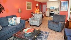 Una sala de estar con un sofá, sillones, una mesa de centro y una cocina al fondo.
