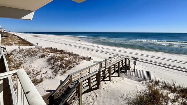 A beach view with a wooden boardwalk leading to the shore, clear skies, and calm ocean waves. - Harbor House B4 2 Bedroom Condo by RedAwning (Gulf Shores)