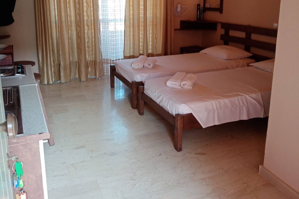A hotel room with two beds, a desk, a mirror, and a window with curtains.