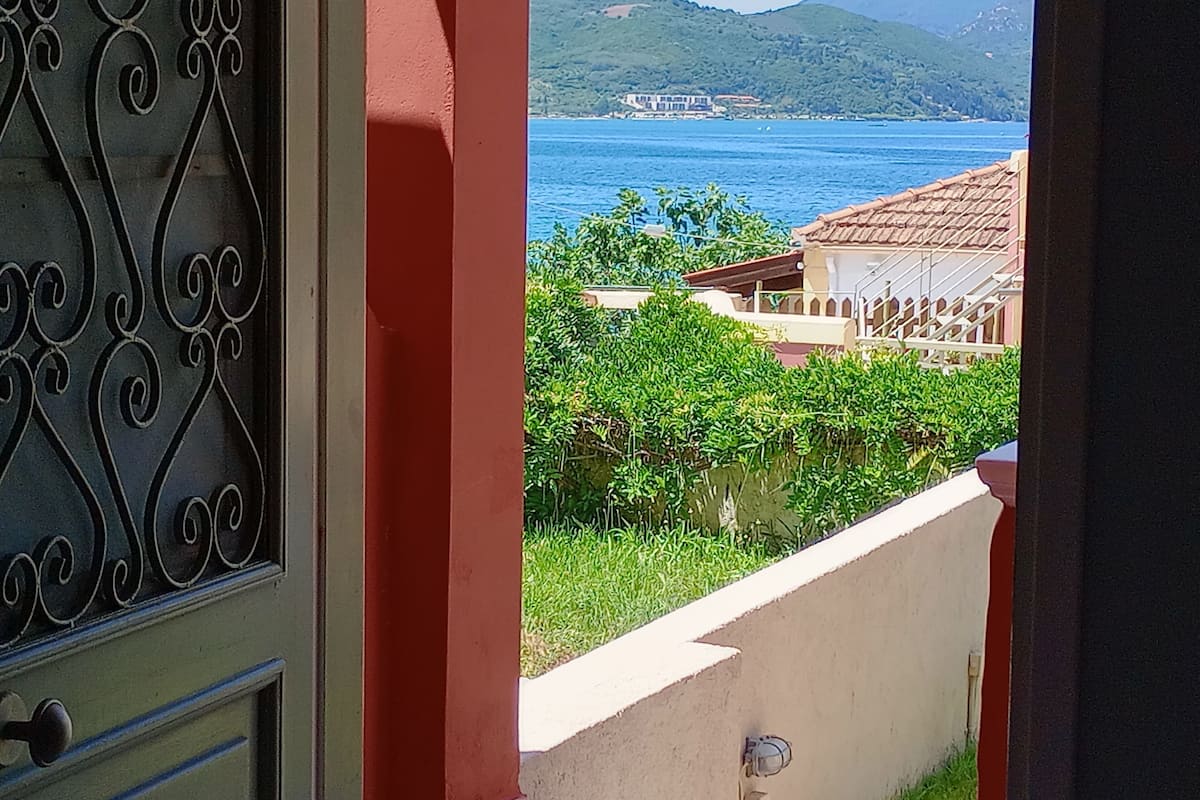 A view from a balcony with a metal gate, a white wall, and a green hedge.