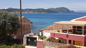 Una zona residencial costera con casas, un mar azul cristalino y colinas al fondo.