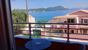 Un balcón con mesa y sillas, con vista a una zona costera con edificios y un mar azul y despejado.