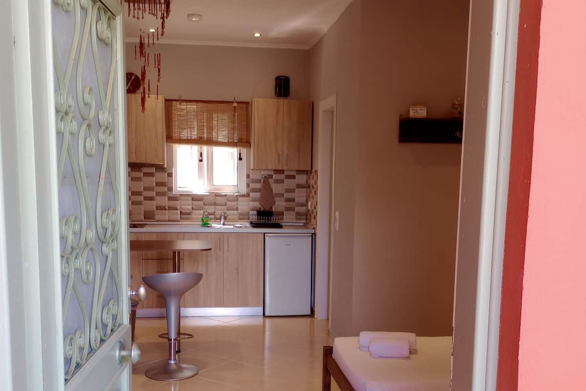 A compact kitchen with a sink, a small refrigerator, and wooden cabinets. There is a dining area with a bench and a small table.