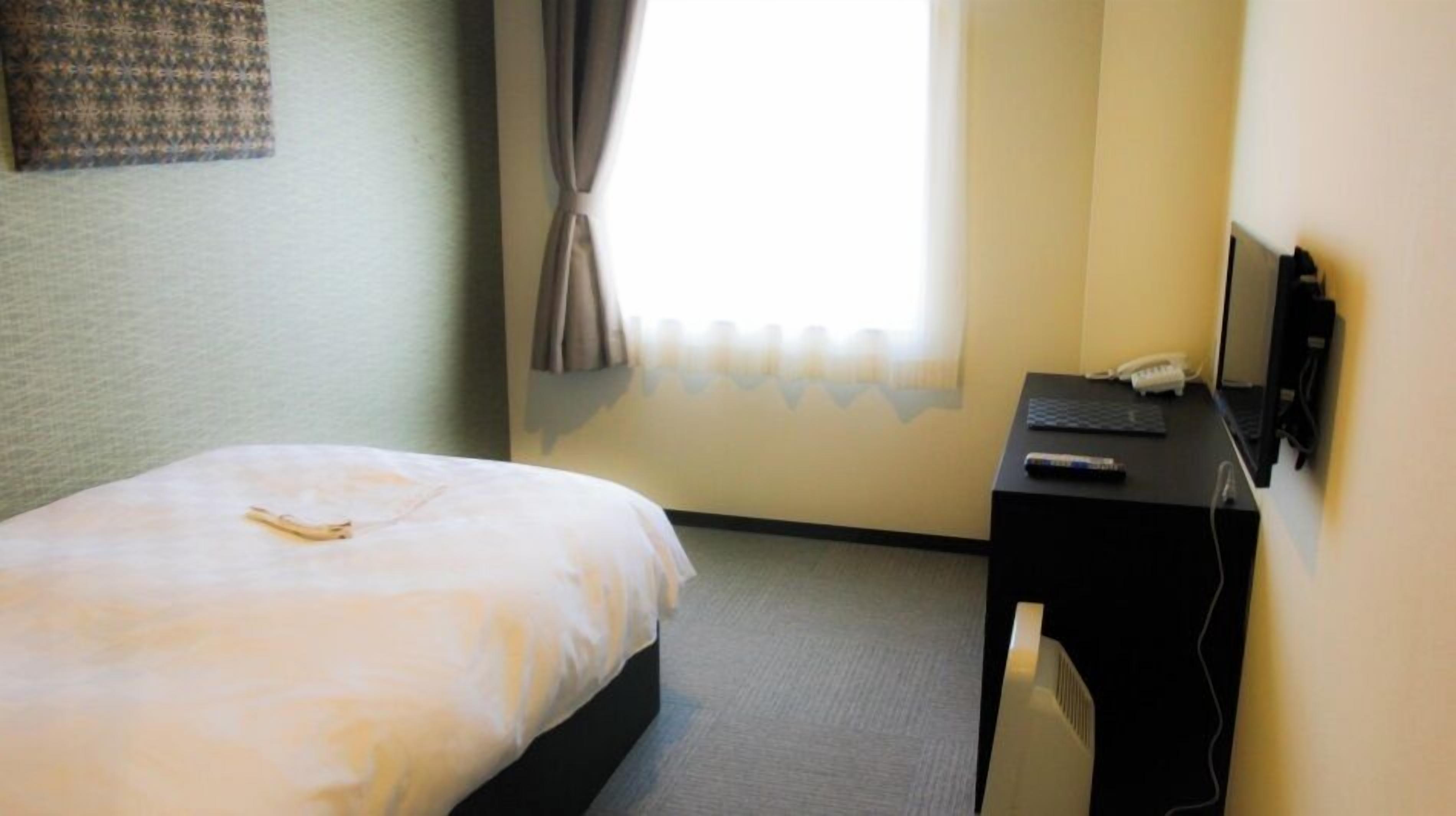 Une chambre d’hôtel équipée d’un lit, d’un bureau avec un ordinateur portable, d’un téléphone et d’une télévision.