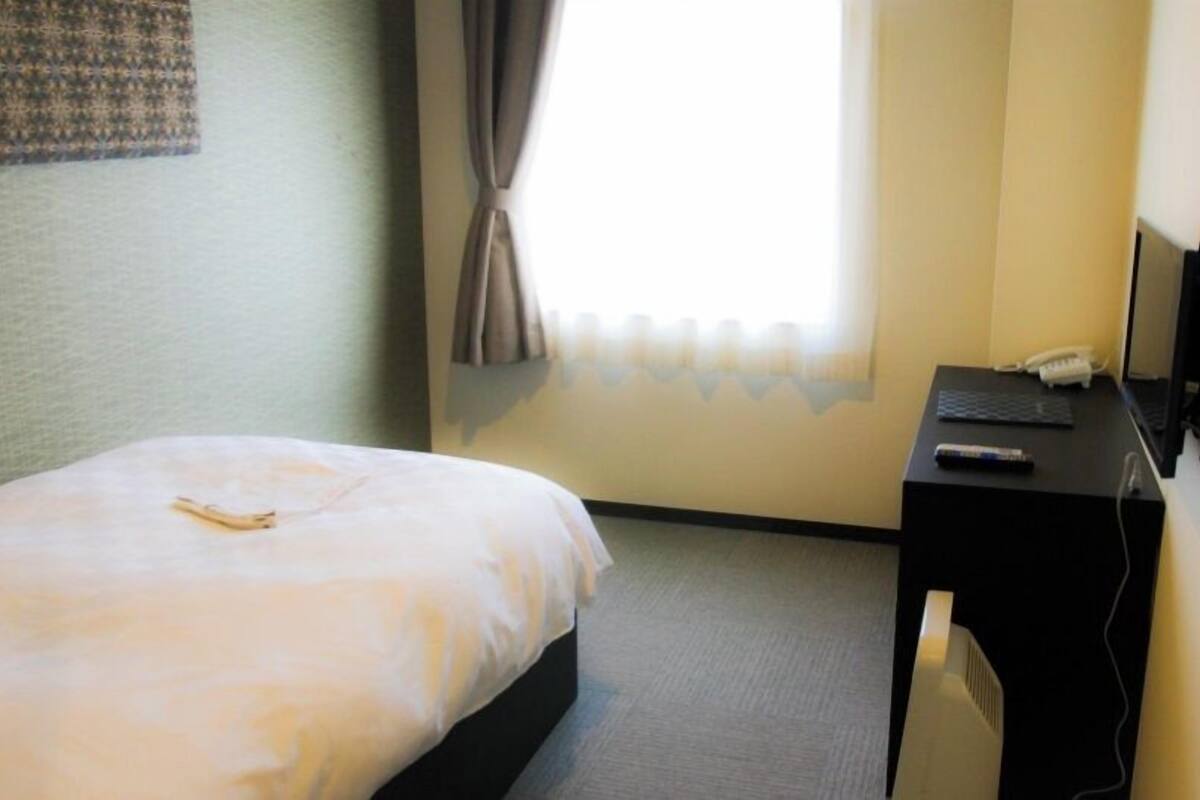 Una habitación de hotel con una cama, un escritorio con una computadora portátil, un teléfono y un televisor.