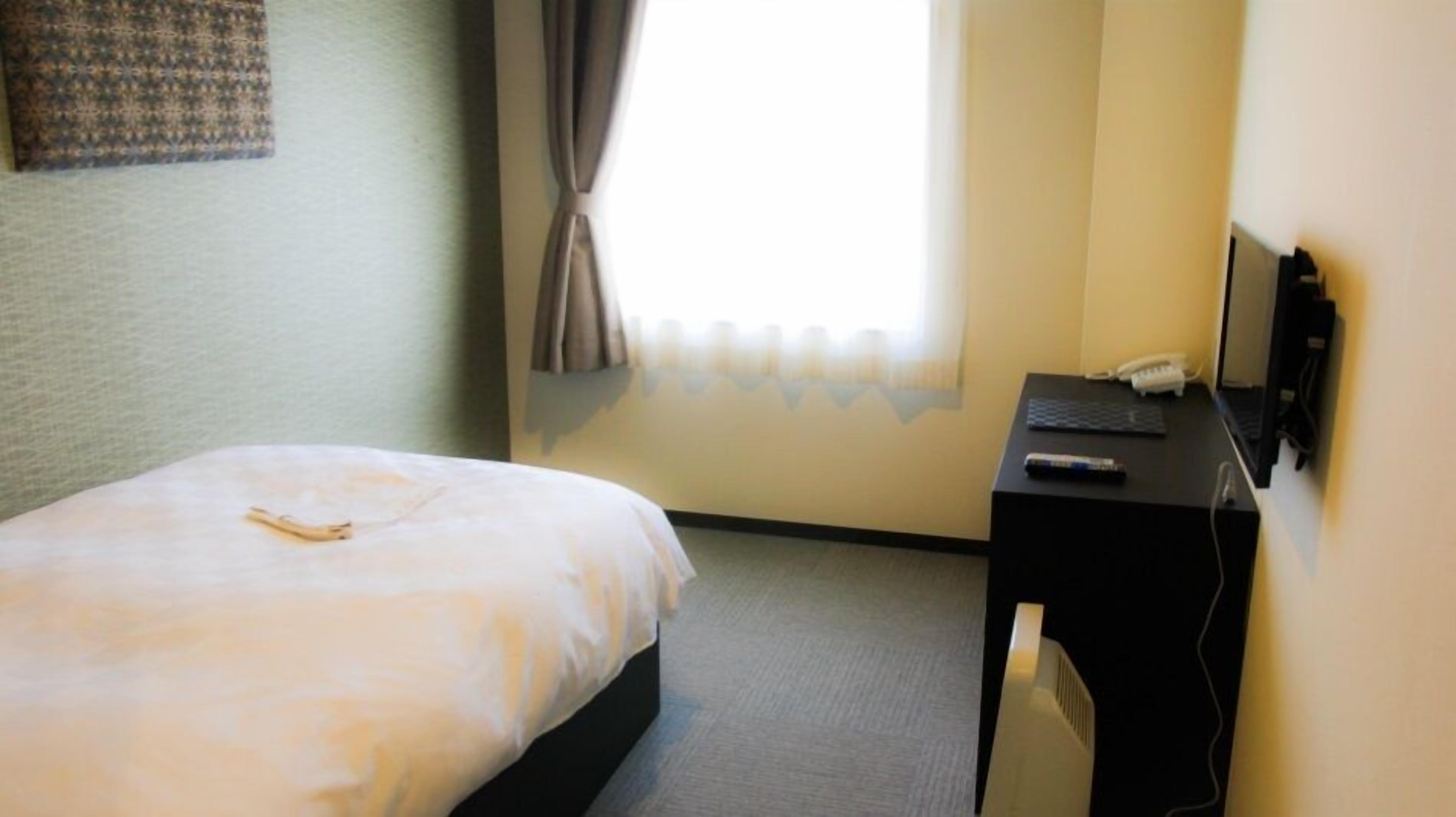 Une chambre d’hôtel avec un lit, un bureau avec un ordinateur et une fenêtre avec des rideaux.