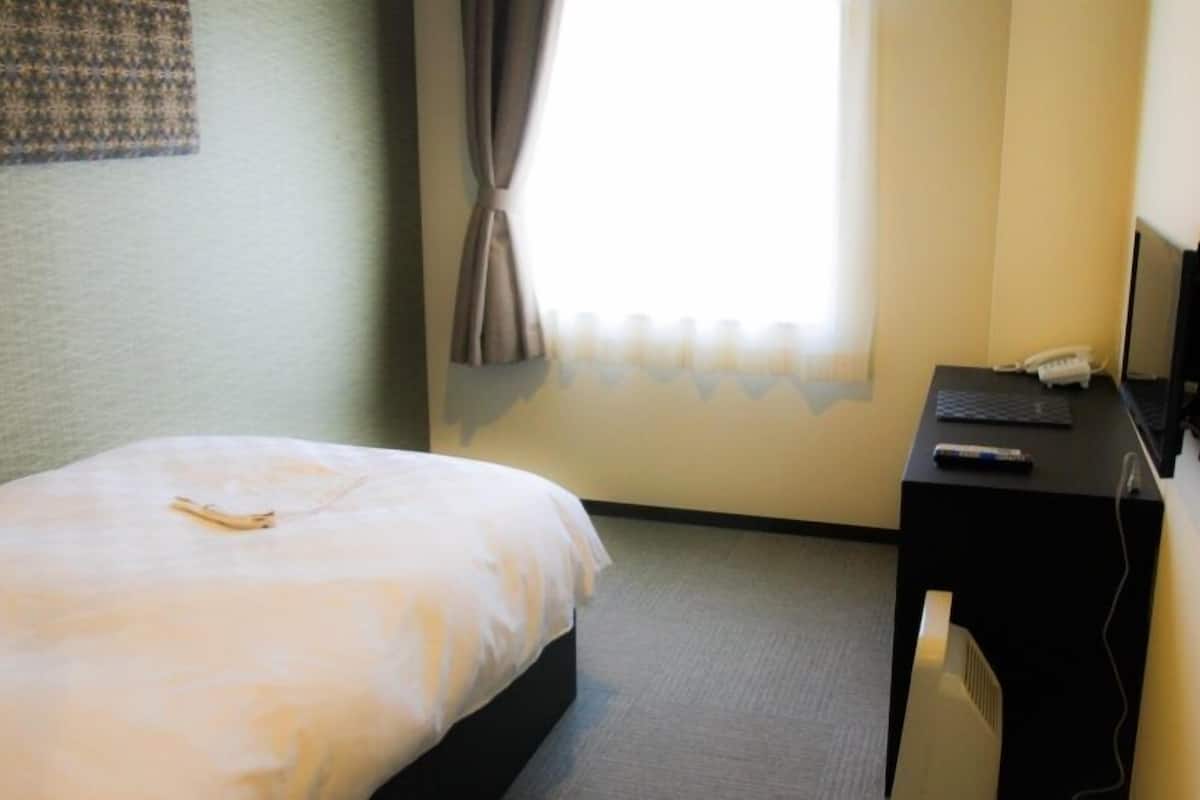 Una habitación de hotel con cama, un escritorio con computadora y una ventana con cortinas.