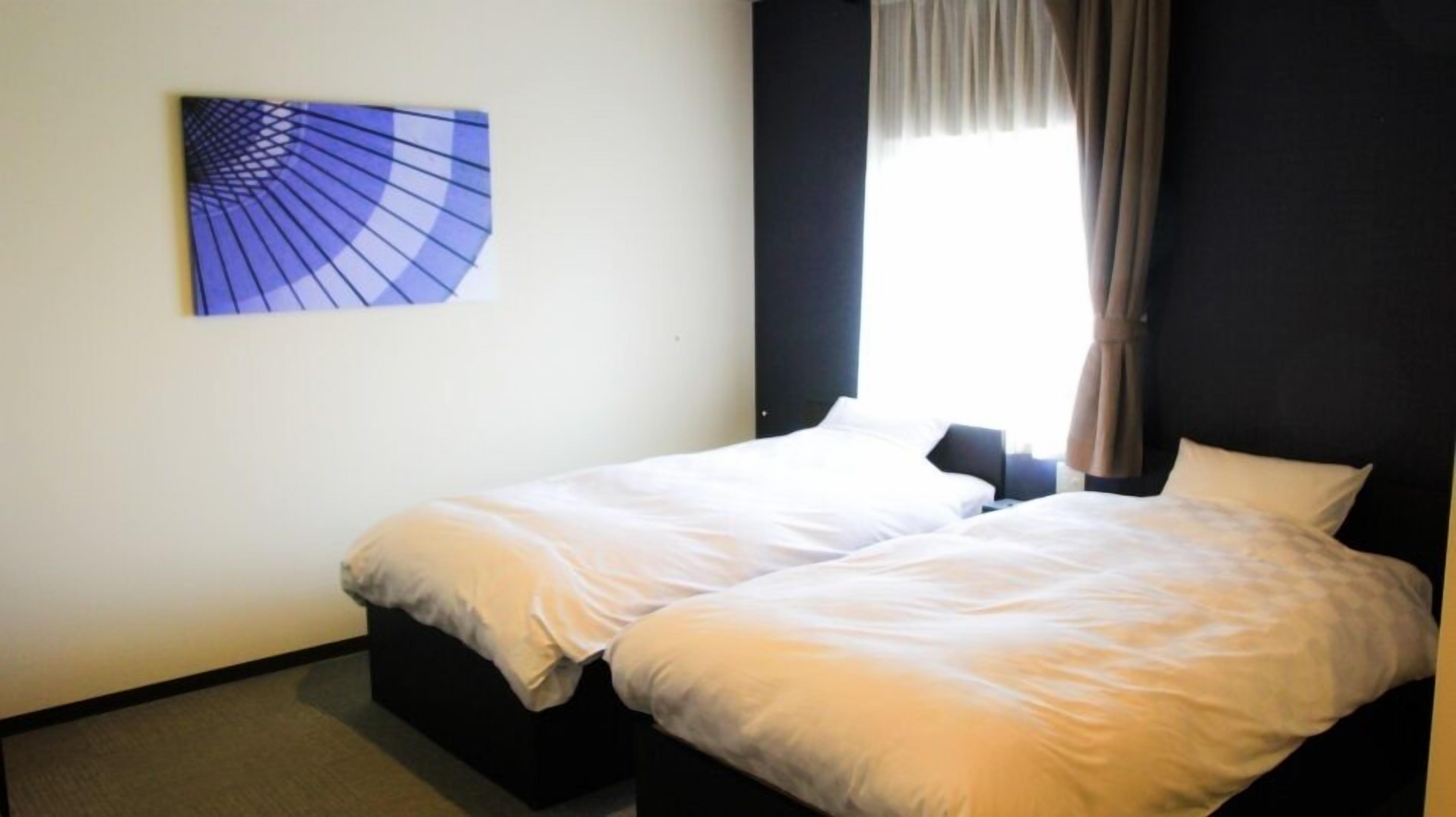 Une chambre d’hôtel avec deux lits simples, une fenêtre avec des rideaux et une œuvre d’art accrochée au mur.