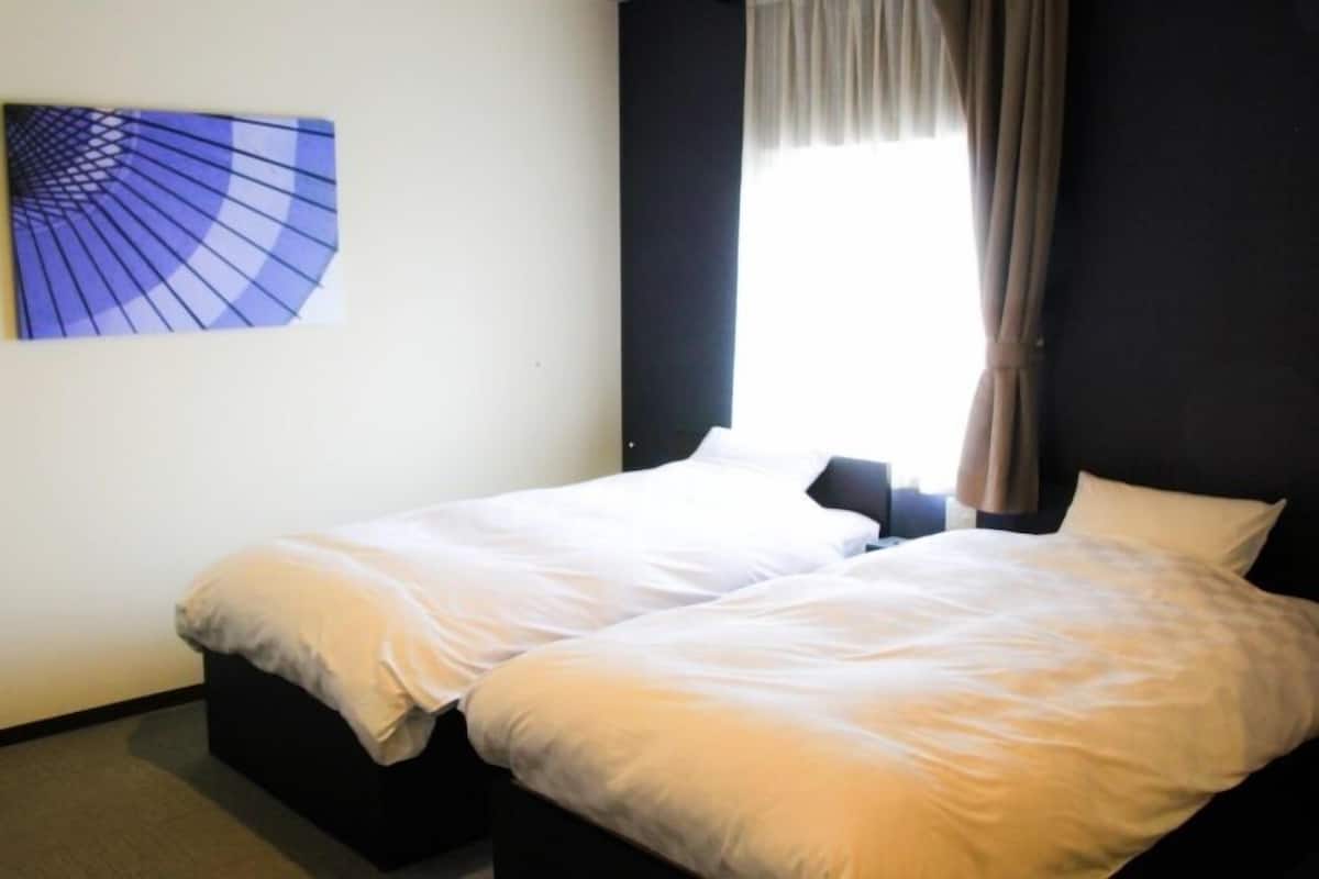Una habitación de hotel con dos camas individuales, una ventana con cortinas y una obra de arte colgada en la pared.