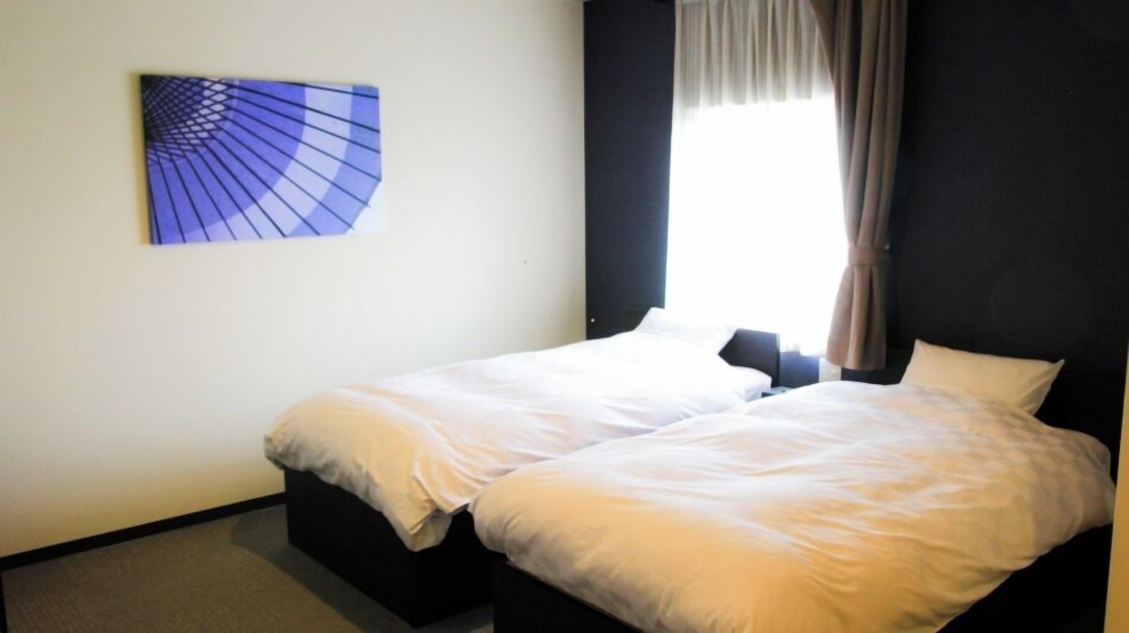 Une chambre d’hôtel avec deux lits simples, une fenêtre avec des rideaux et une œuvre d’art accrochée au mur.