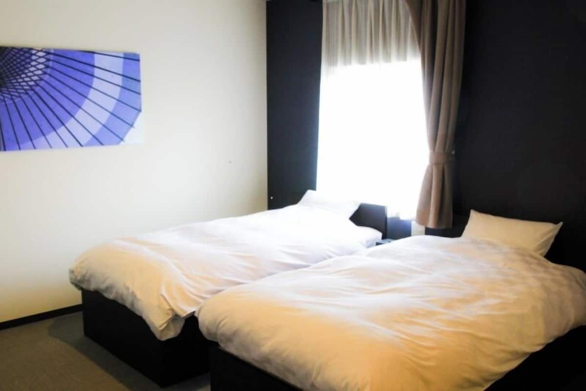 Habitación de hotel con dos camas individuales, una ventana con cortinas y una obra de arte colgada en la pared.