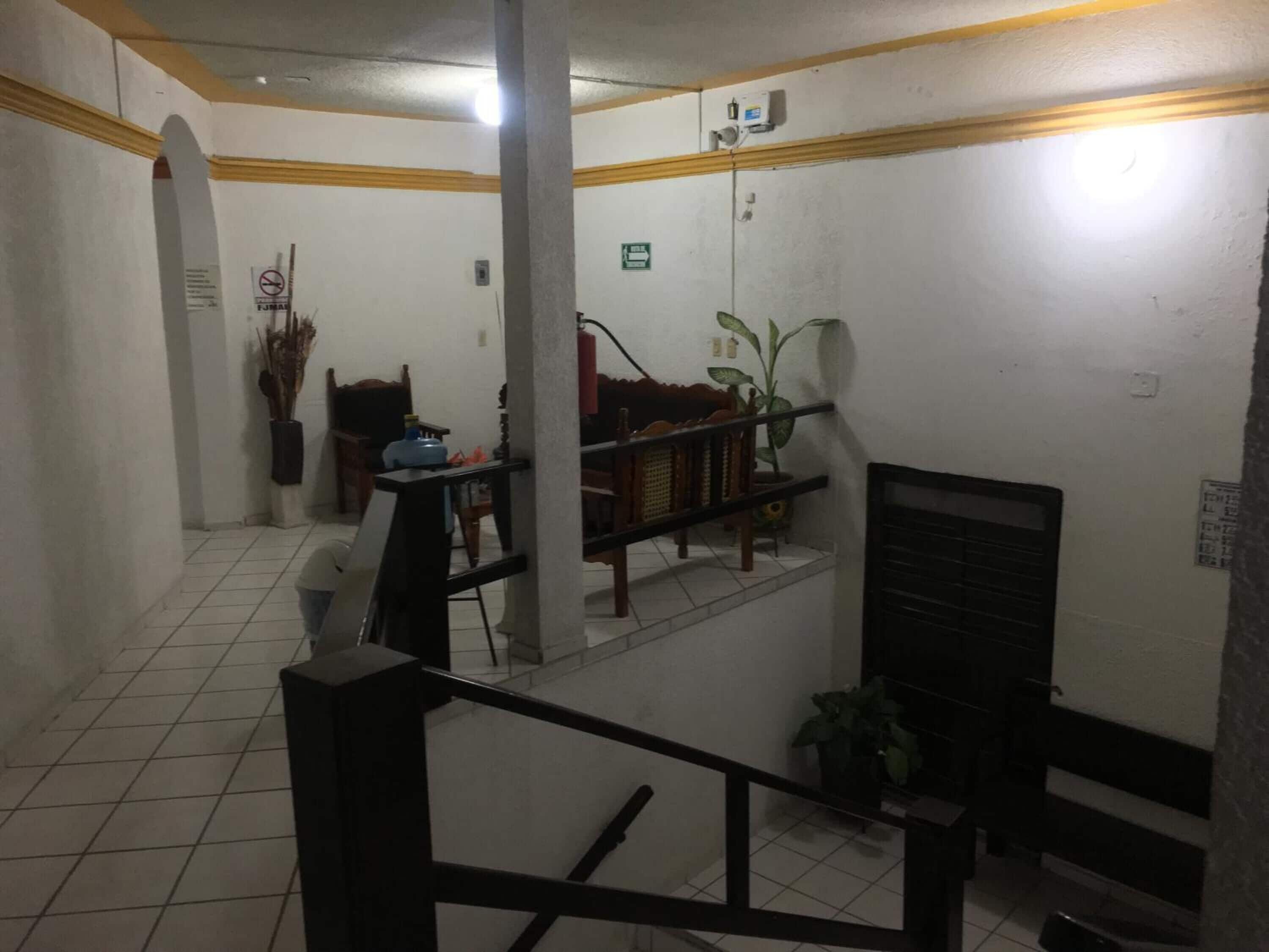 A hotel lobby with a tiled floor, a staircase, a reception desk, and a seating area with chairs and a table.