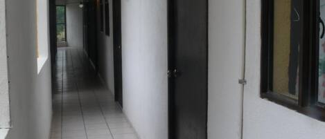 A corridor with tiled flooring, a black door, and a wall-mounted light fixture.