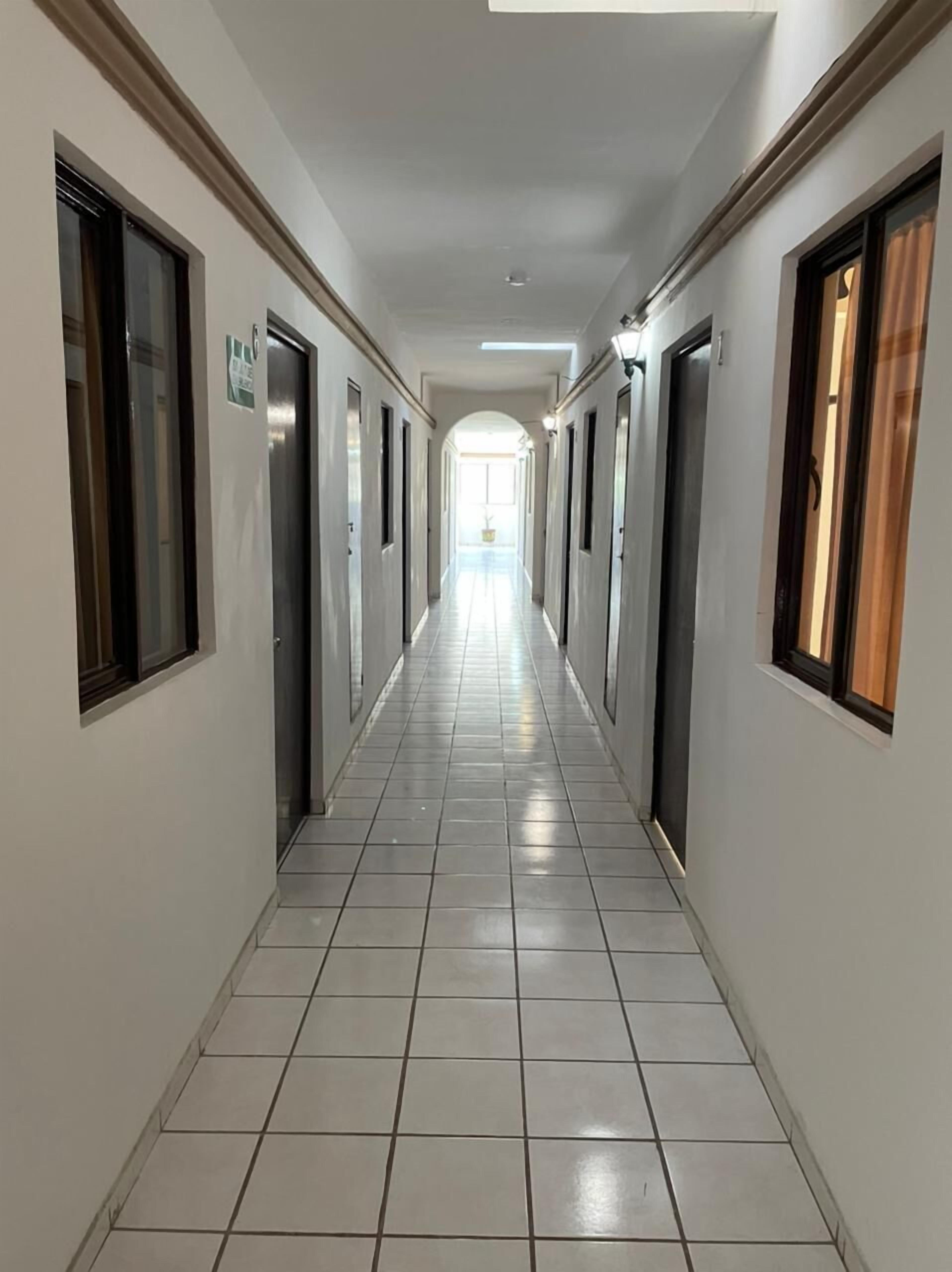 A long, narrow hallway with doors on both sides, tiled floor, and a bright ceiling.