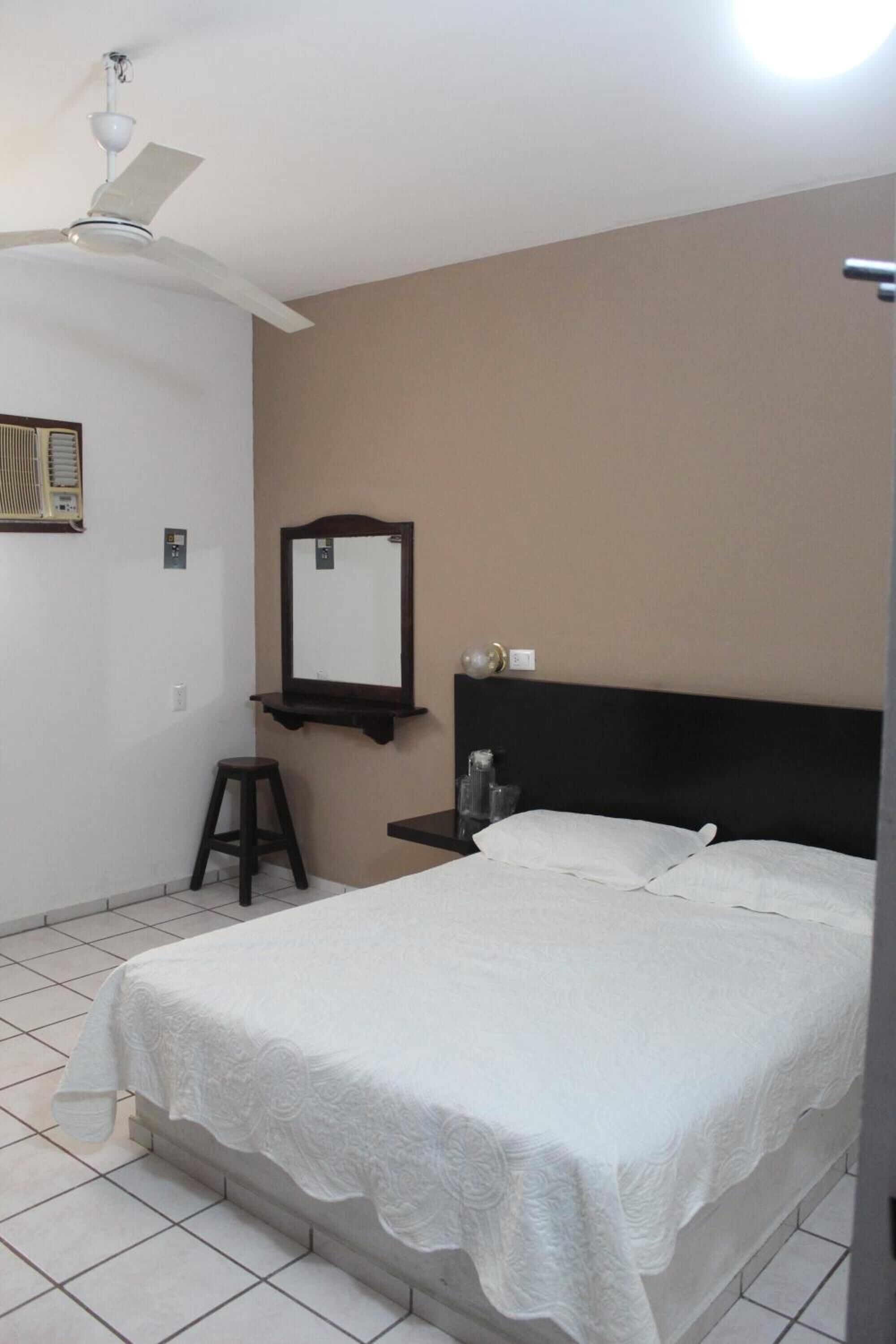 A bedroom with a bed, a ceiling fan, a mirror, and a small stool.