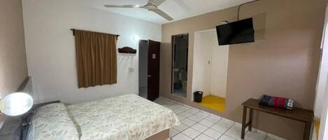 A bedroom with a bed, a ceiling fan, a TV mounted on the wall, a small table, and a door leading to another room.