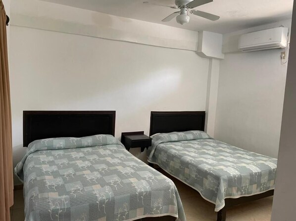 A room with two beds, each with a headboard, a nightstand, and an air conditioning unit mounted on the wall.