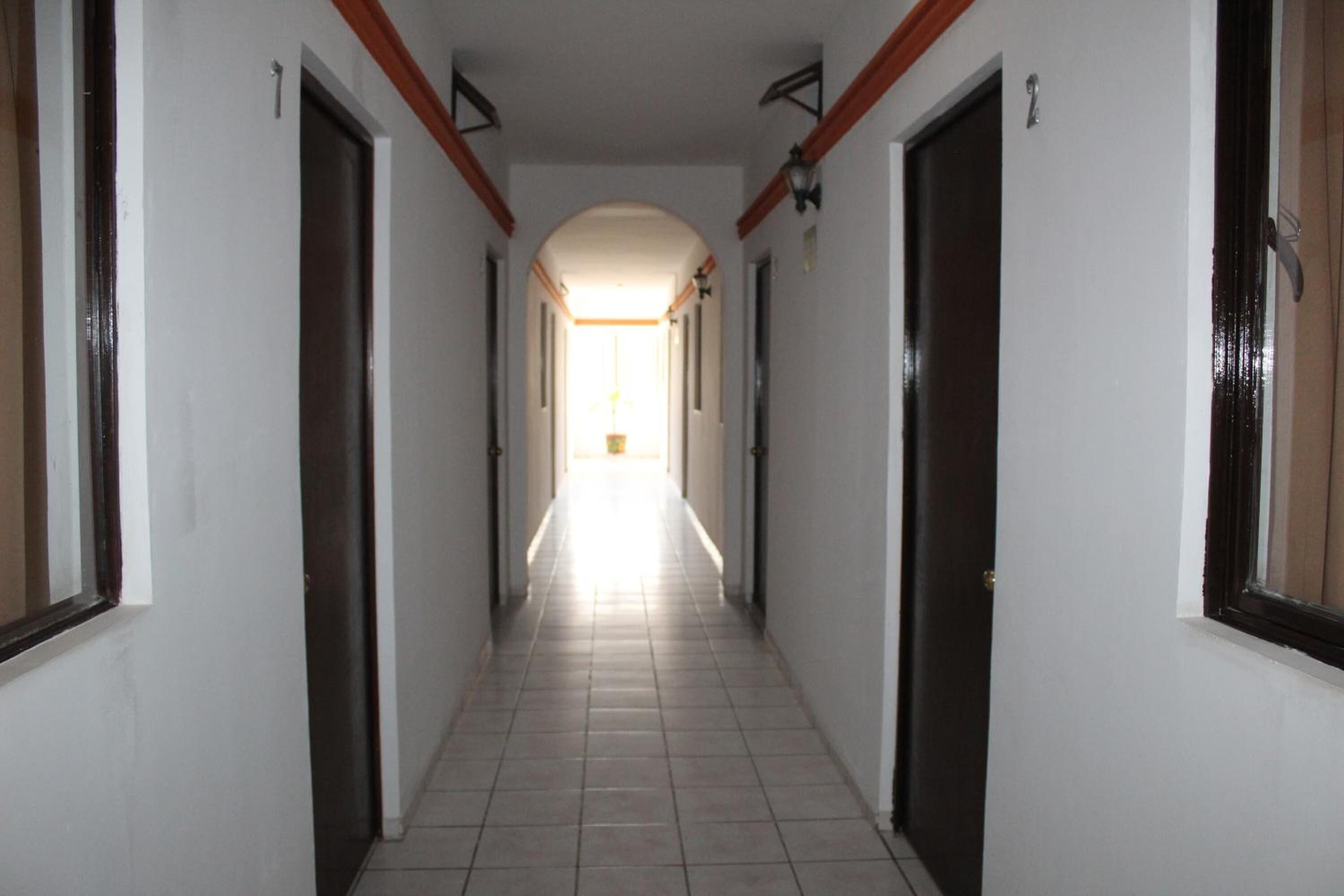 Un pasillo largo y estrecho con puertas a ambos lados, que conduce a una habitación luminosa al final.