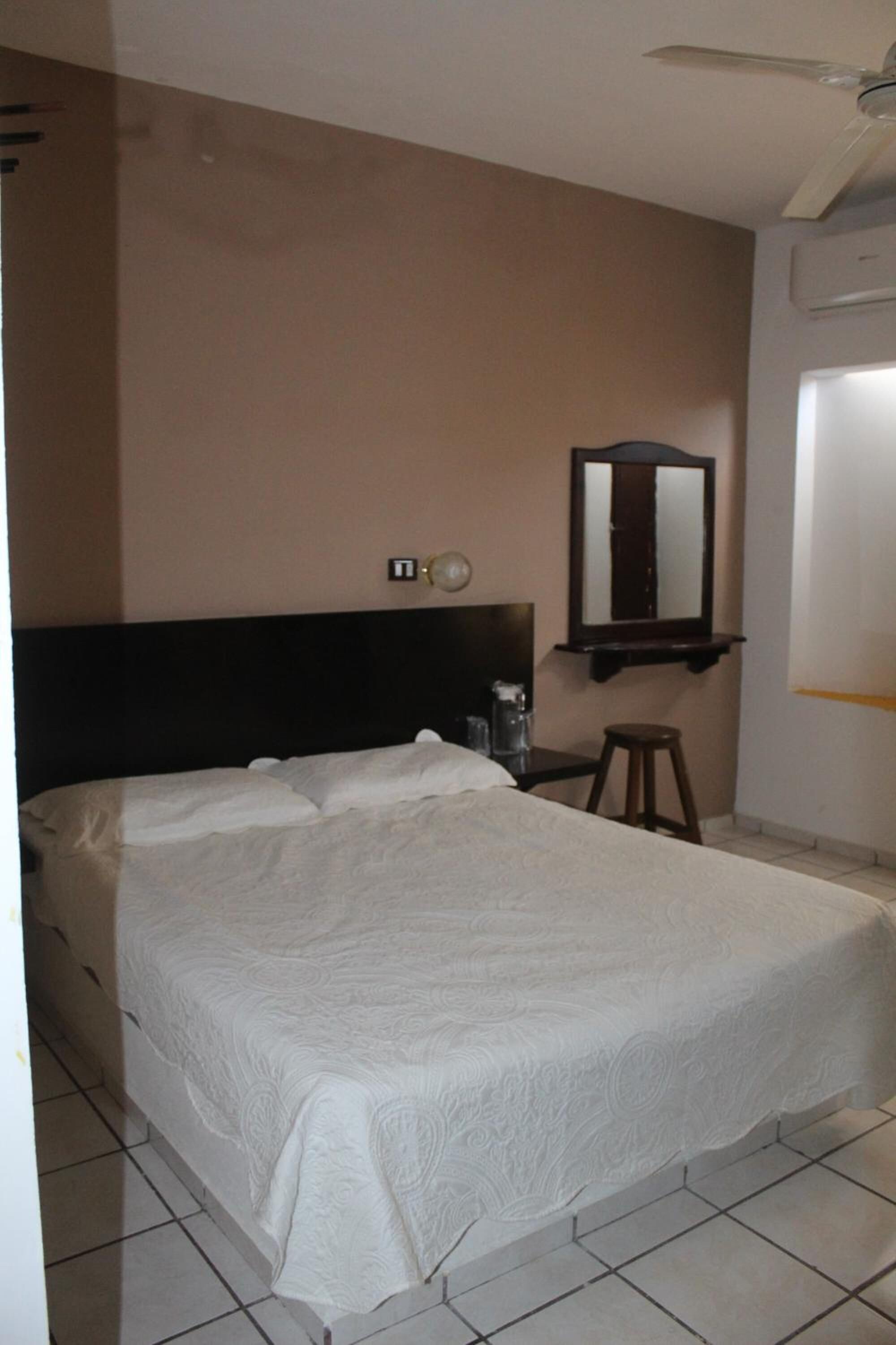 Un dormitorio con una cama grande, un ventilador de techo, un espejo y una ventana.
