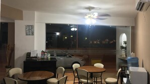 A dining area with a round wooden table and six chairs, a black counter with a menu, and a large window with a view of the night cityscape. - Hotel Moreno (Ciudad Valles)