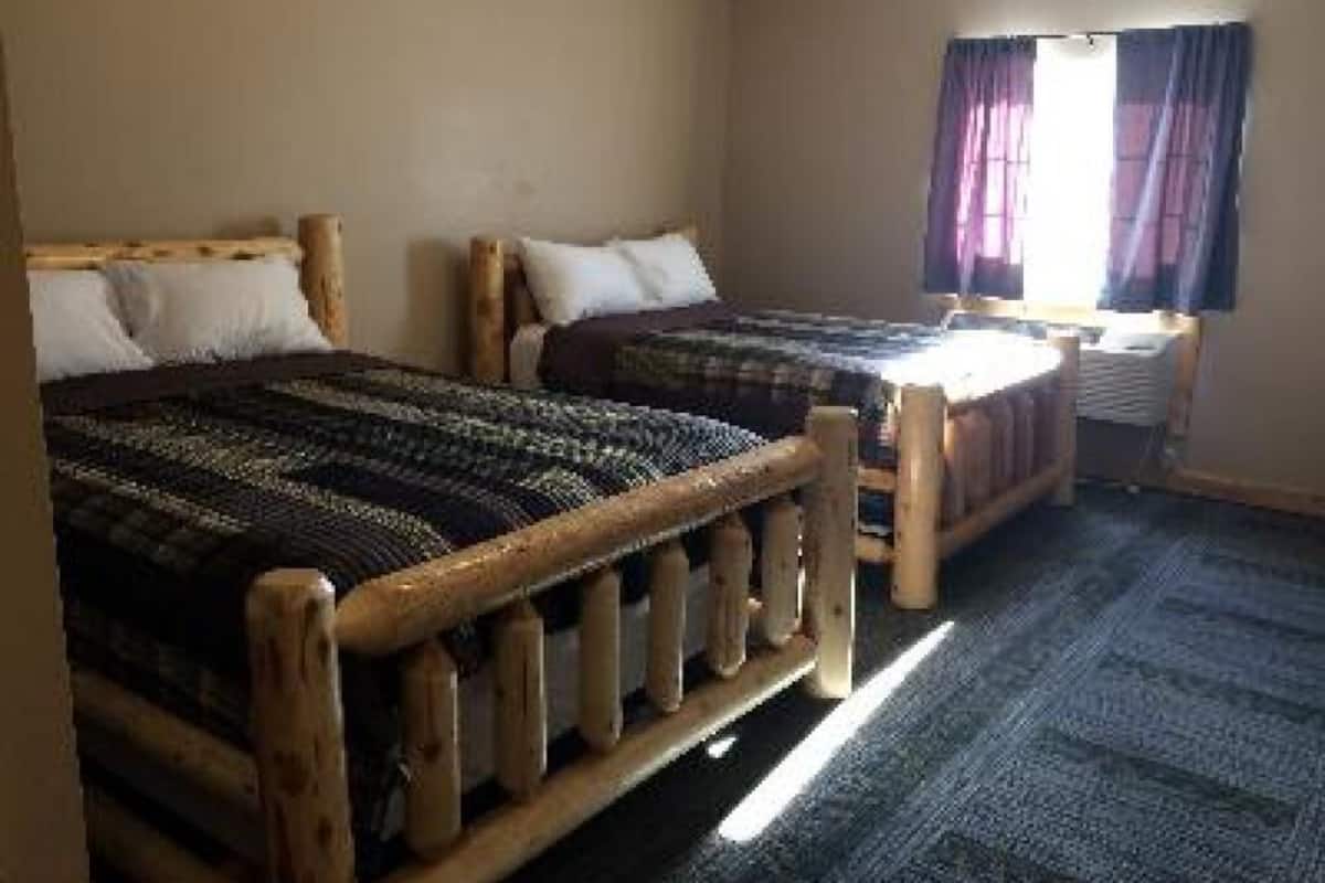 A room with two wooden beds, a window with curtains, and a carpeted floor.