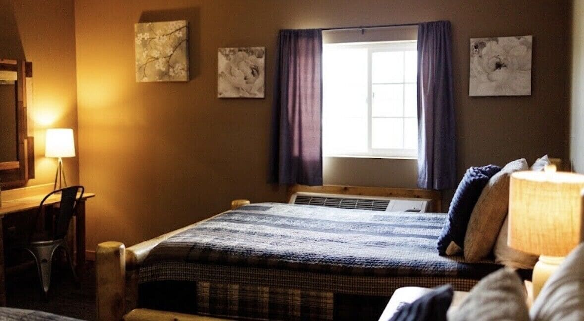 A bedroom with a bed, a desk, a chair, and a window with curtains.