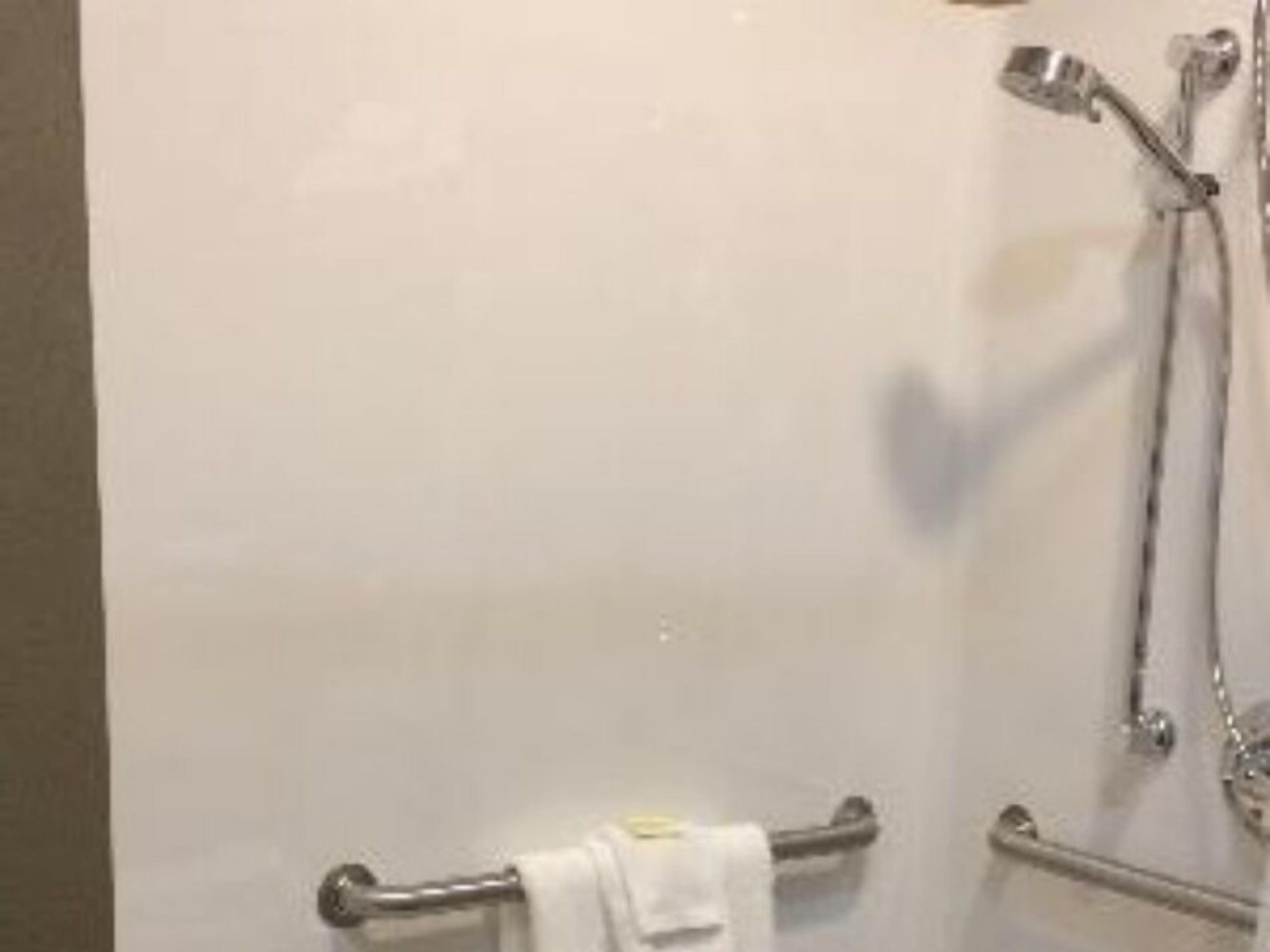 Un baño con ducha, toallero y barra de apoyo.