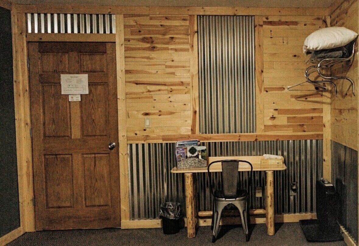 Une petite pièce avec une porte en bois, une table avec une chaise, un radiateur et un coussin posé sur une étagère.