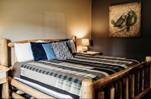 A wooden-framed bed with a striped blanket, a pillow, and a wall-mounted lamp. - Big Horse Inn and Suites (Lewistown)
