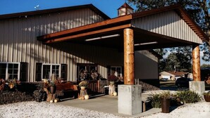 Un bâtiment doté d’un porche couvert soutenu par des colonnes en bois, d’une fondation en briques et d’une façade en métal.