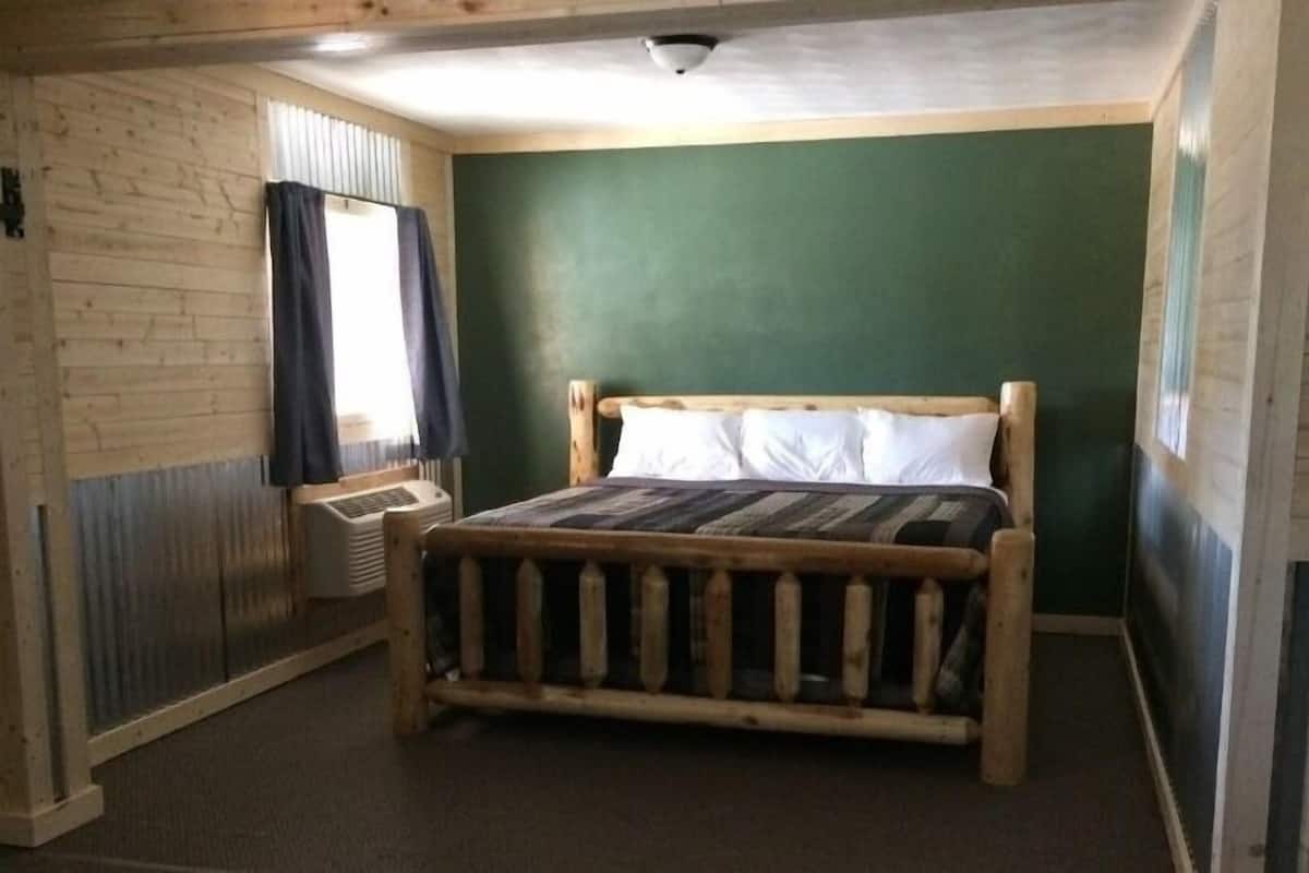 A room with a wooden bed, a window with curtains, and a green wall.