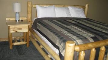Una cama de madera con cubrecama a cuadros, una mesita de noche de madera con una lámpara, y suelo alfombrado.