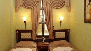 Habitación de hotel con dos camas, una ventana con cortinas, lámparas de pared e imagen enmarcada en la pared.