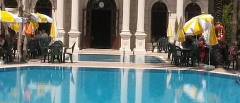 A swimming pool with a decorative edge, a statue of a horse rider, and a building with columns in the background.