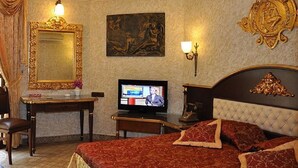 Habitación de hotel con un espejo grande y decorativo, un televisor, una cama con ropa de cama roja y una obra de arte colgada en la pared.