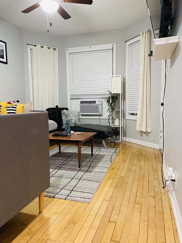 A living room with a sofa, a coffee table, a ceiling fan, and a window with blinds.