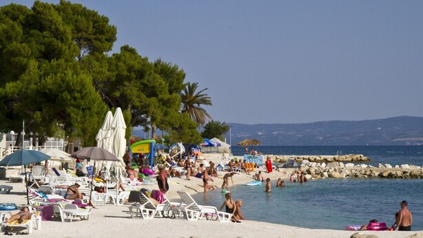 A beach with sun loungers, umbrellas, and people swimming.