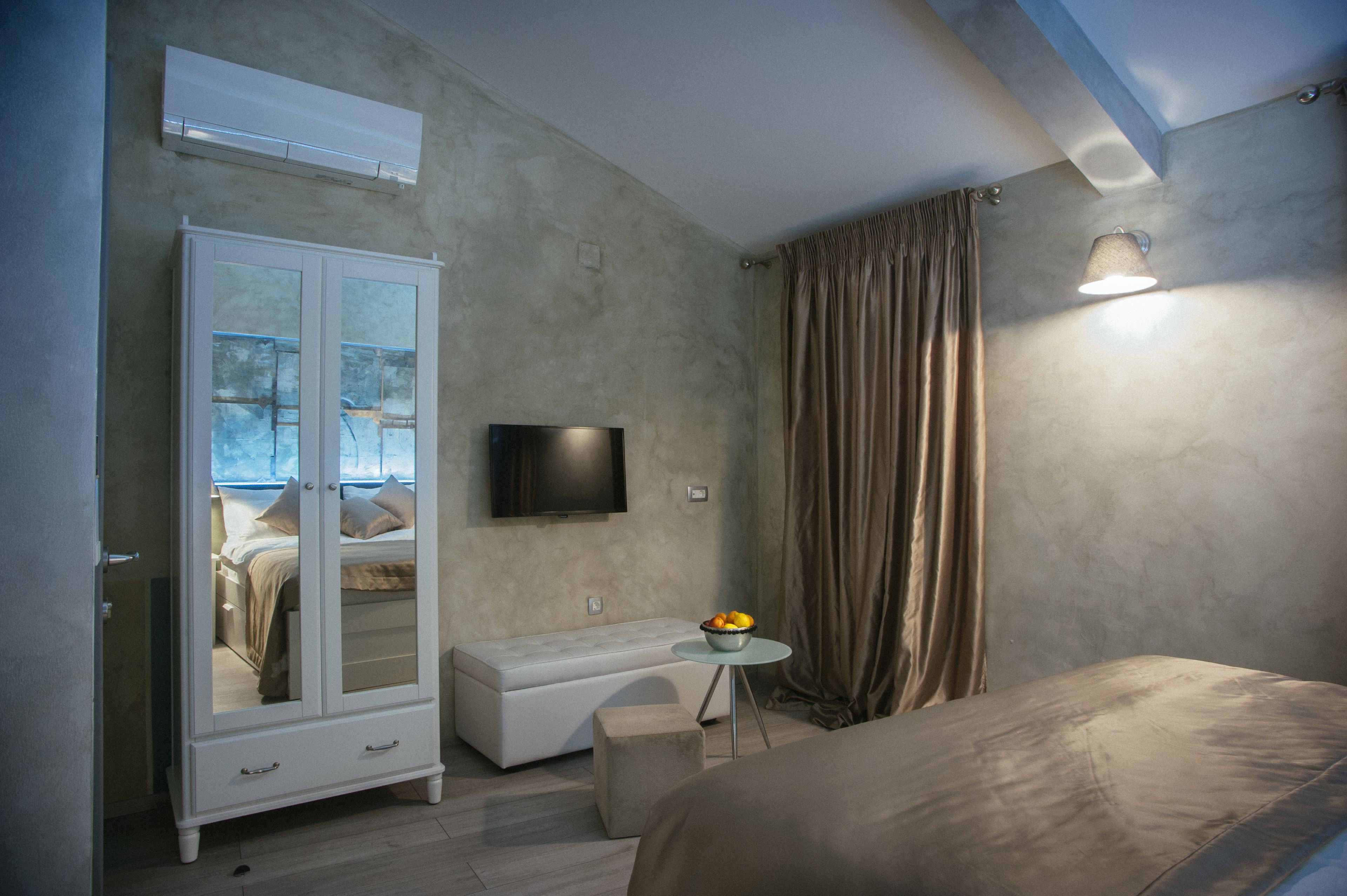 Een slaapkamer met een bed, een kledingkast, een televisie, een klein tafeltje met een fruitschaal, en een raam met gordijnen.