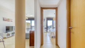 A hallway leading to a bedroom with a bed, a chair, and a TV in the adjacent room.