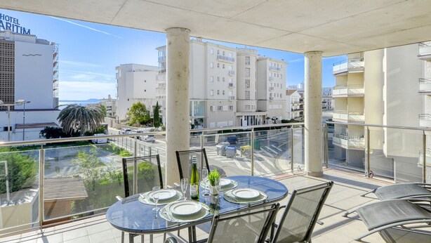 A balcony with a glass table set for dining, overlooking a cityscape with buildings and a palm tree.