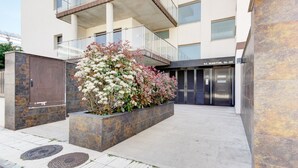 A modern building entrance with a planter of flowering shrubs, a metal gate, and a building name sign.