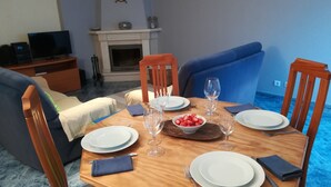 A dining area with a wooden table set for four, surrounded by blue sofas and wooden chairs. - Sesimbra Holiday Apartment (Sesimbra)